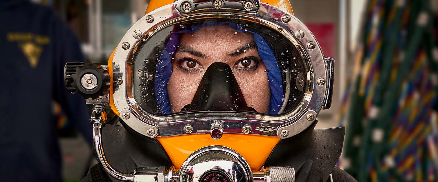 Close-up of a Navy Medical Officer wearing a diving helmet, captured in a moment of intense concentration before a dive.