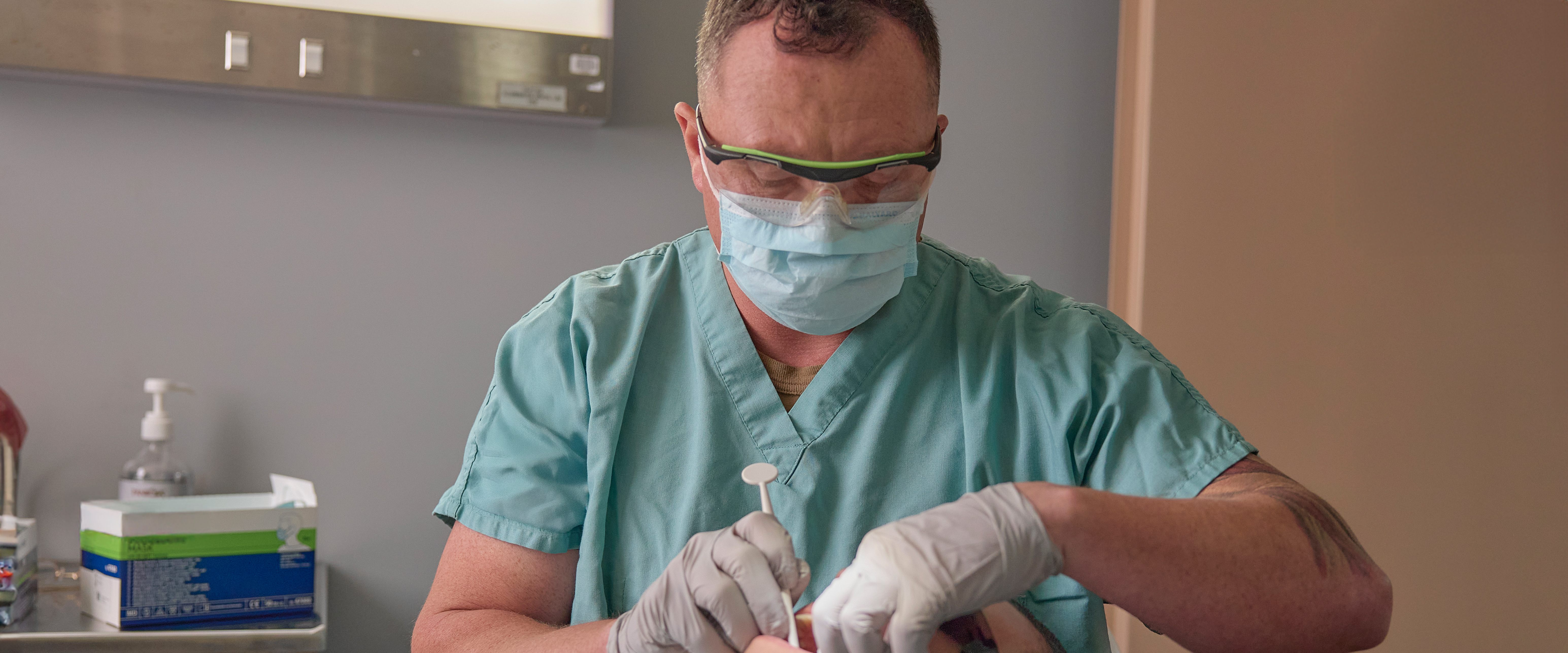 Navy dentist performing a dental procedure on a patient in a clinic setting.