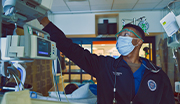 Navy nurse wearing a face mask and face shield adjusting a patient monitoring device in a hospital room. 