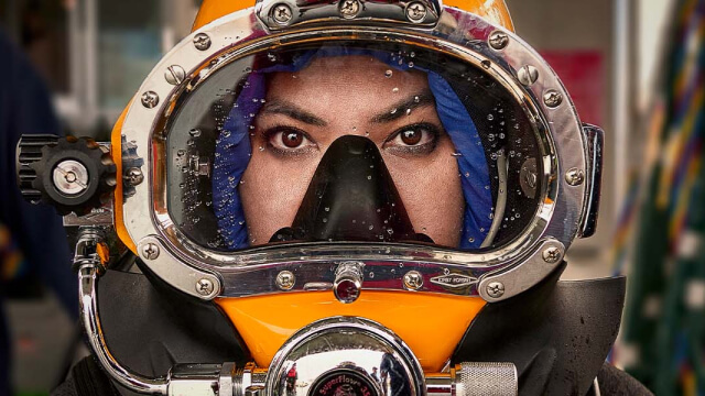 Close-up of a Navy Medical Officer wearing a diving helmet, captured in a moment of intense concentration before a dive.