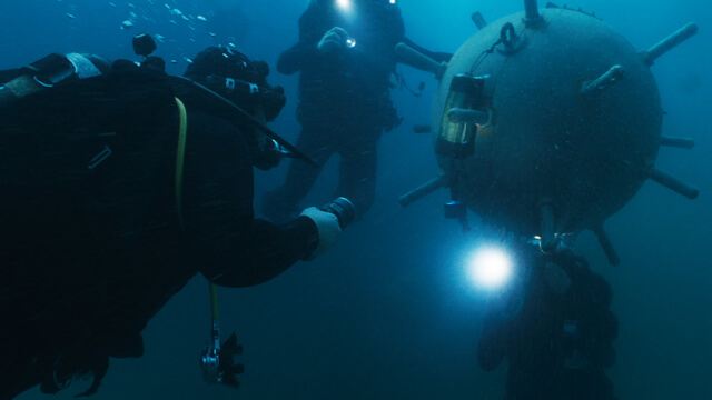 Explosive Ordnance Disposal Technicians inspect an underwater mine using specialized diving gear and expertise to ensure safety and mission success.